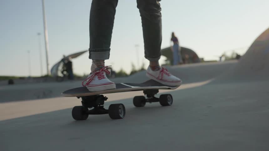 Skateboarder wearing white shoes skateboards in a skateboard park outdoors on a sunny day