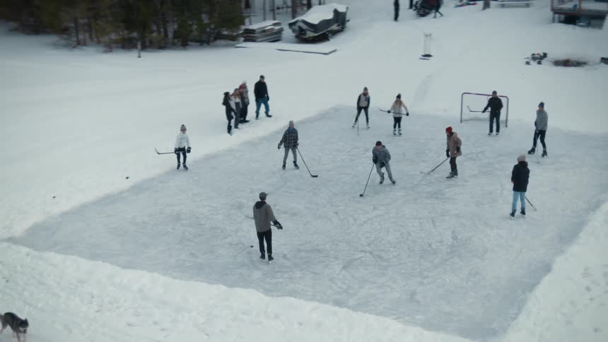 A group of people are outside playing hockey on a winter day and others are watching