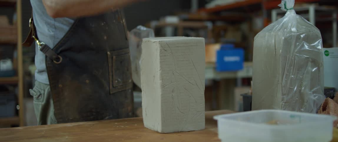 A man takes a block of clay out of a bag and sets it on a table and walks away