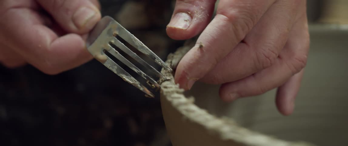 An artist uses a fork to put a pattern on pottery