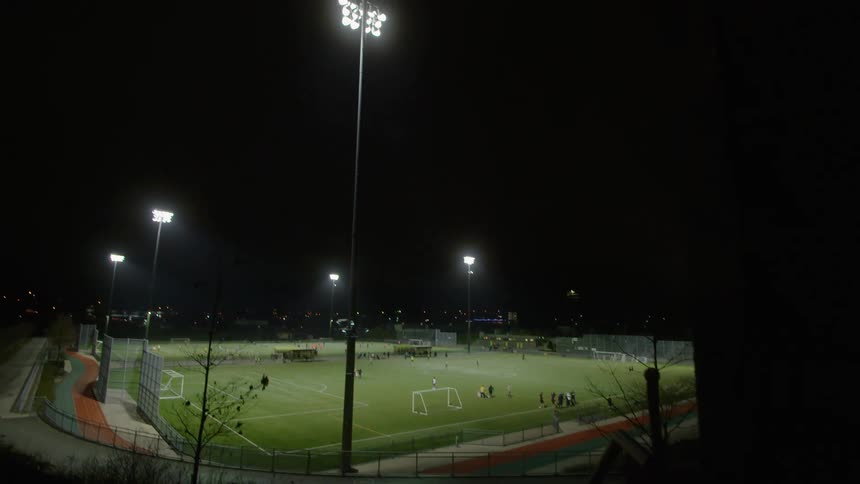 Distant view of football field with footballers playing football at night
