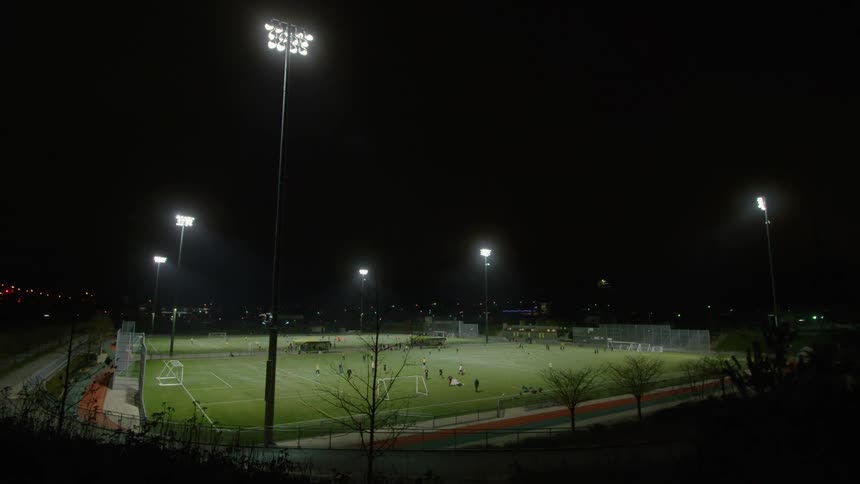 Two teams playing a soccer match on a field in the city at night
