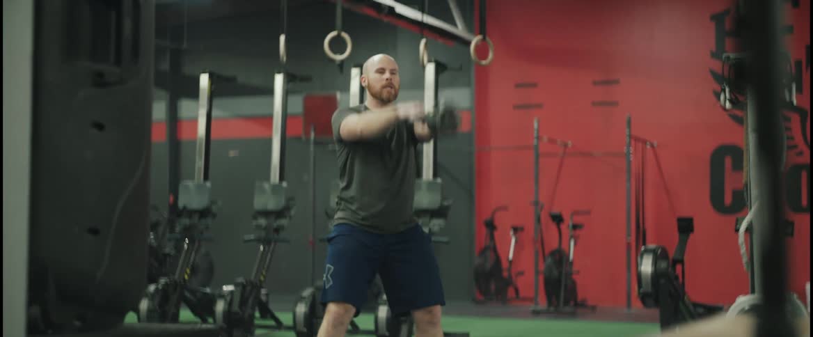 Bald man with beard t shirt and blue shorts works out with kettlebell in the gym