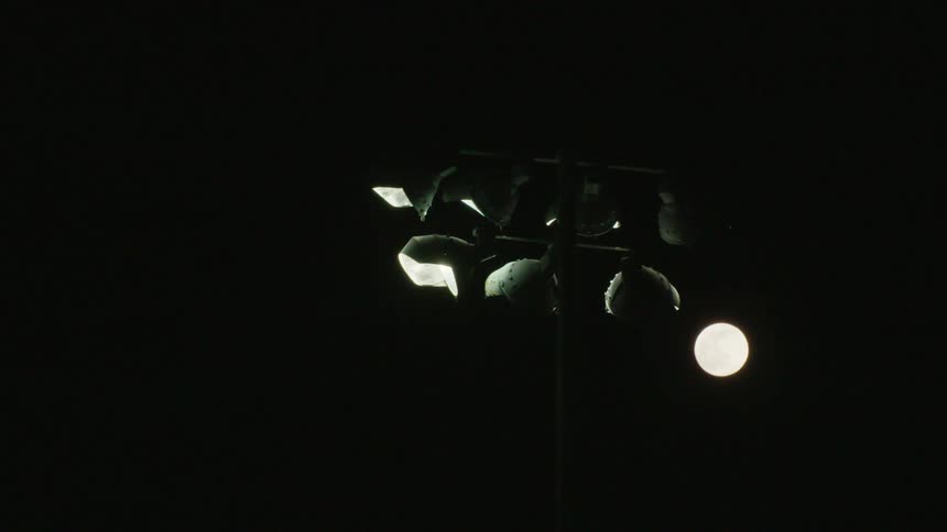 A stadium light with a full moon glowing in the sky