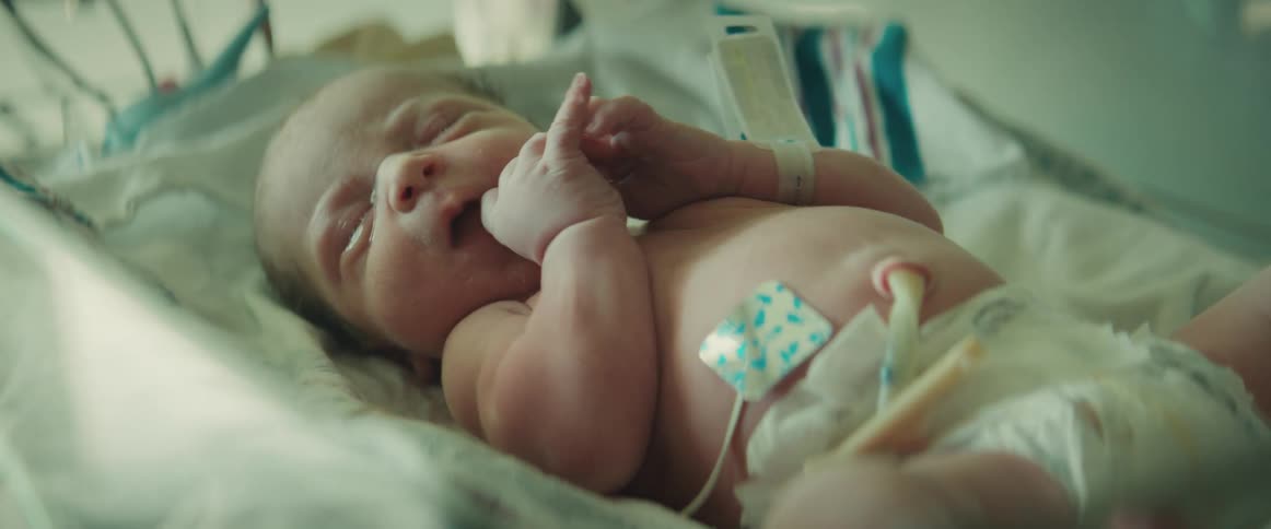 A newborn baby with its umbilical cord still attached lies in a bed
