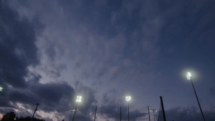 Several flood lights are positioned beneath a cloudy sky at dusk