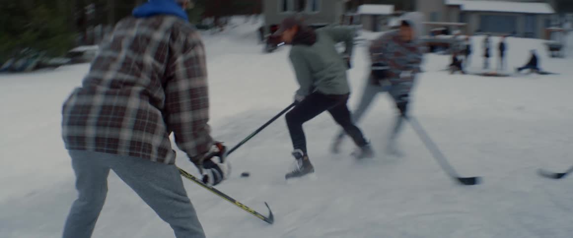 A group of people play ice hockey together on a patch of ice in a rural area on a winter day