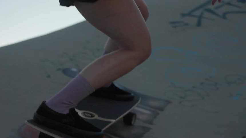 View of girls feet as she is riding a skateboard in a skateboard park