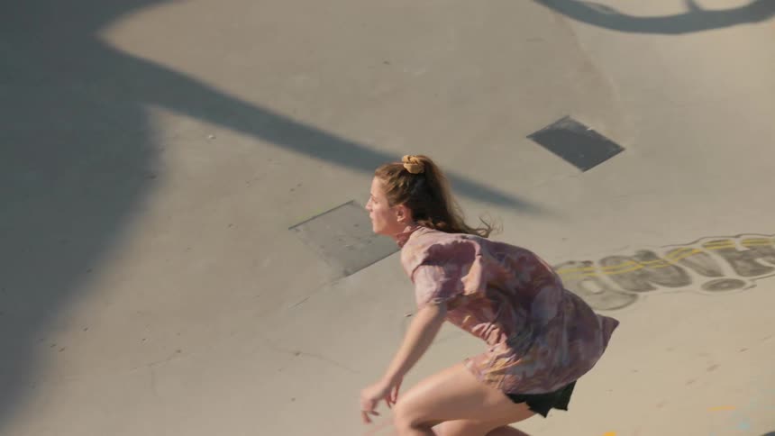 A woman skateboards around and up the side of a graffiti covered bowl at a skatepark