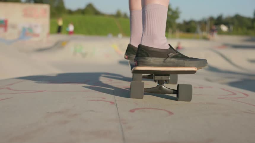 A skateboarder pushes off and skates the bowl at a skatepark on a sunny day