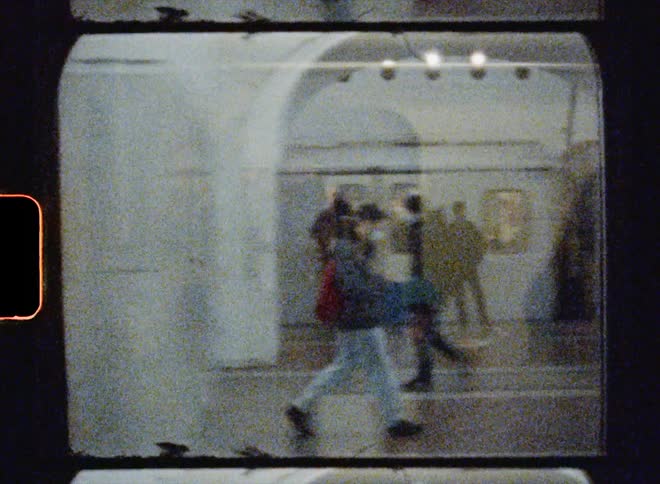 Pedestrians move through train terminal as train cars also flow past