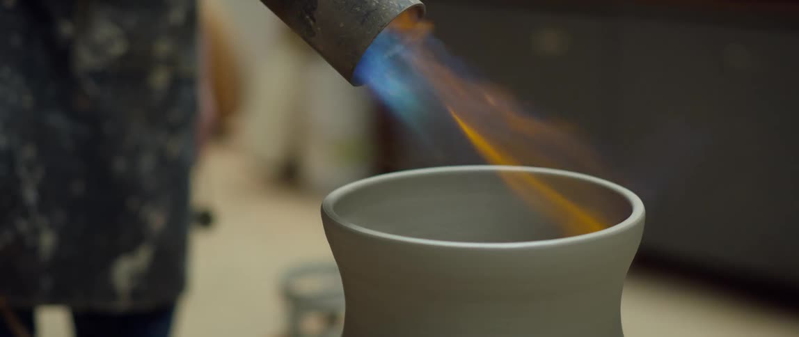 Sculptor uses flames from a torch on a clay vase spinning on a turntable