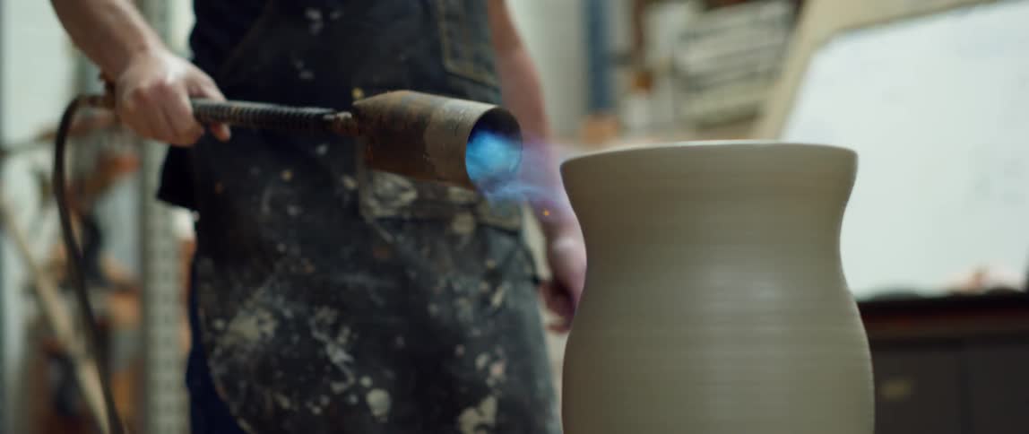 Standing potter fires clay vase using a flaming torch