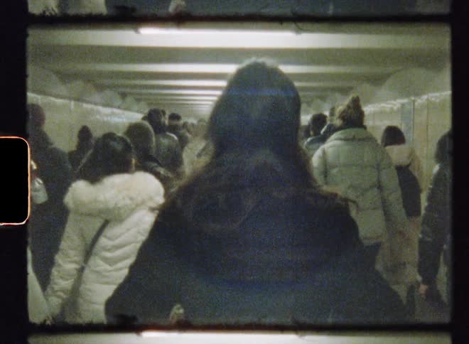 Crowd of people wearing winter coats walk along tiled corridor