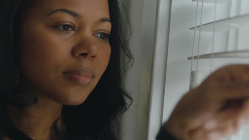 A woman peers through window blinds