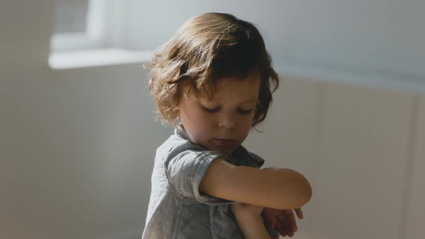 Young child examines vaccination site on their arm and then smiles