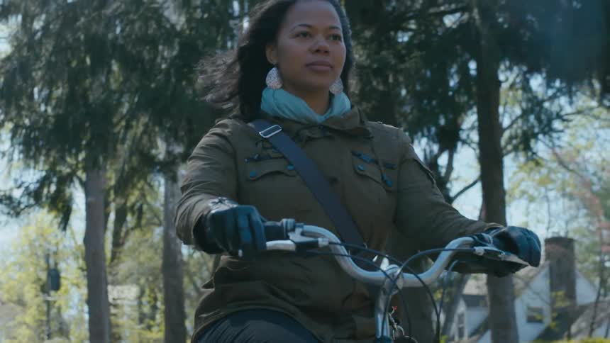 Female cyclist rides past flowering trees in neighborhood