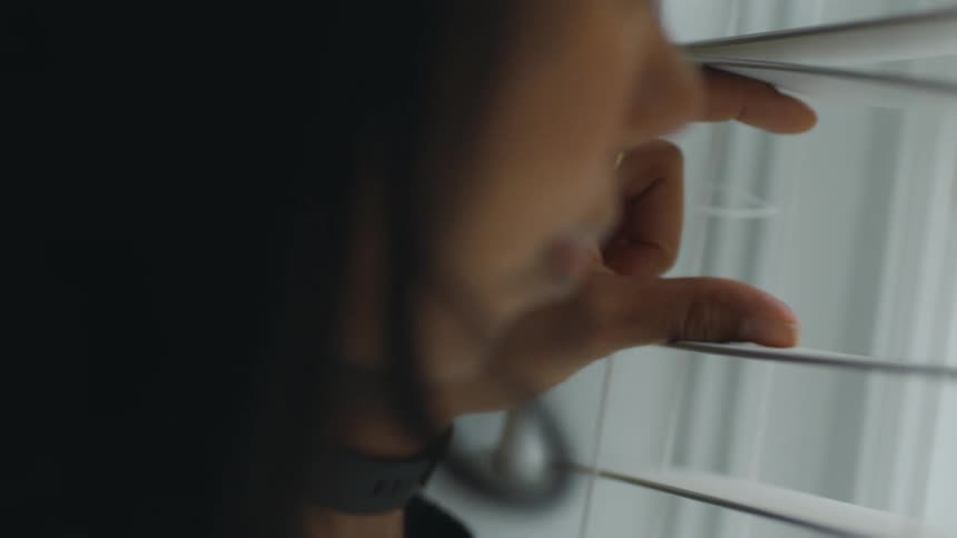 A woman looks through her window blinds