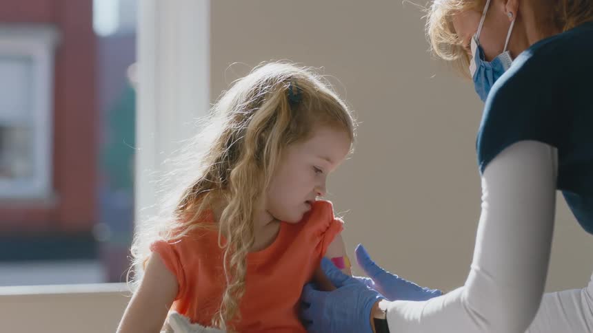 Young girl gets vaccine with stuffed animal and smiles at nurse