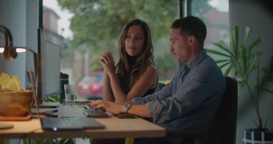 Two people are talking together while typing on a computer