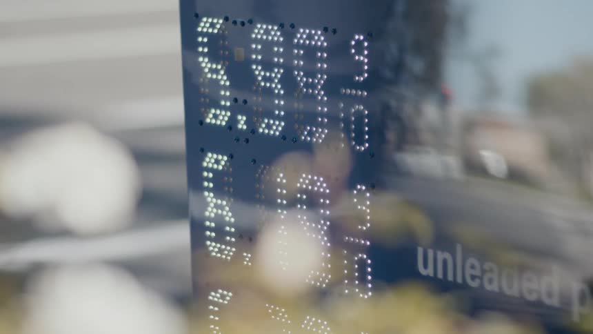 Gas station sign shows gas prices as traffic passes on nearby road