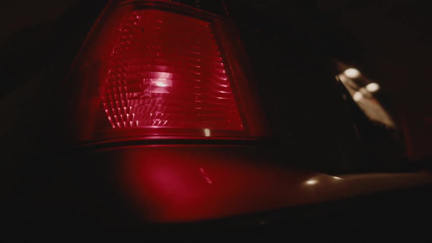 The tail light on an automobile is blinking in the darkness