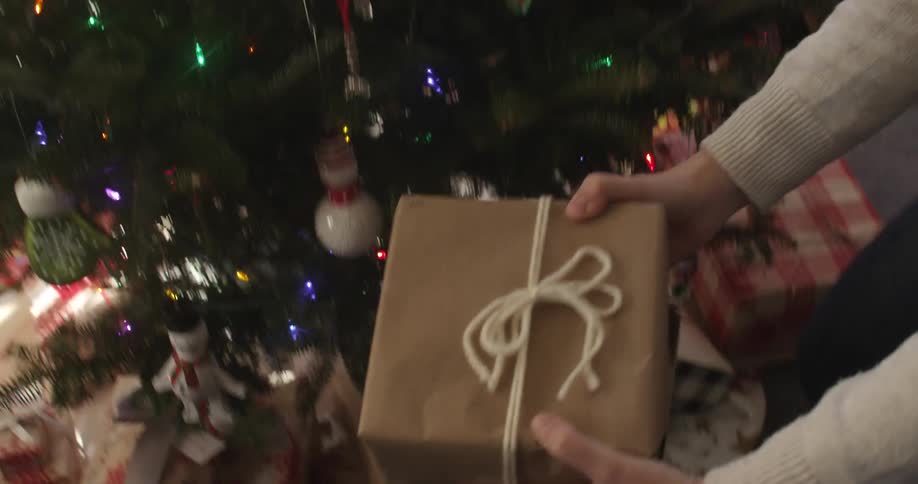 Woman places a wrapped gift under a christmas tree
