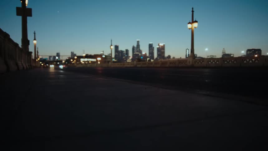 Headlights on cars shine as they travel on a road near downtown and tall buildings and skyscrapers are in the distance