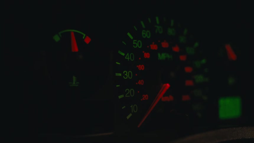 The speedometer and fuel gauge of a vehicle is still visible in low light