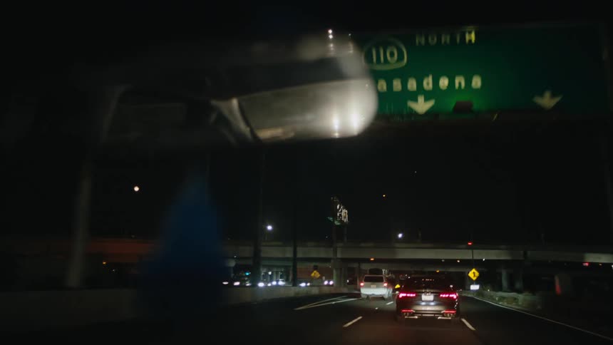 Car drives along highway at night toward city lights and passing under bridges