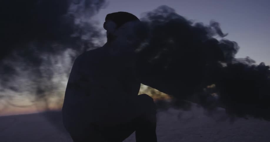 A man is sitting along the coast overlooking the water and holding a smoke flare