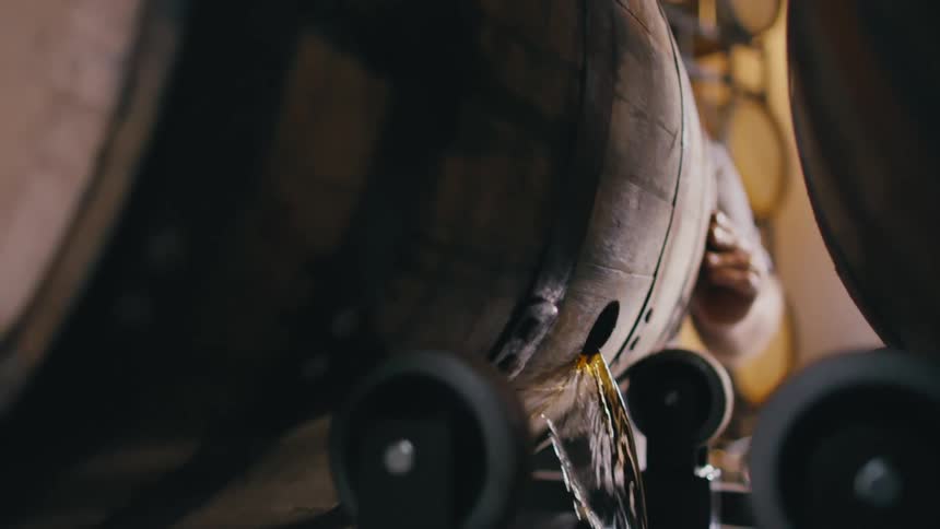 A man in a distillery turns a whisky barrel after whiskey poured out
