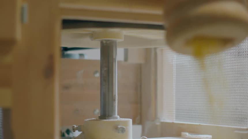 Shaft at base of mill sitting near a window rotates and milled grain flows from spout