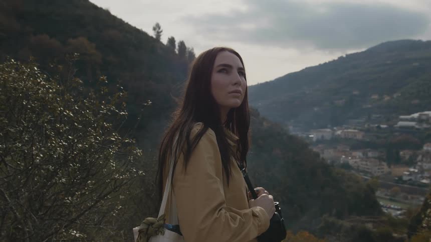 Woman holds binoculars as she stands and looks around at the mountains and valley