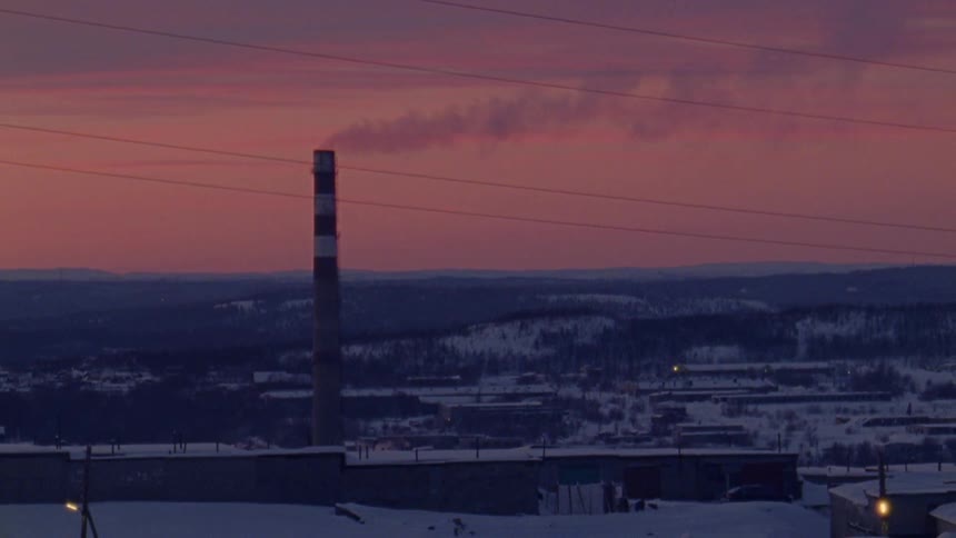 Smoke billows from a tall chimney at a factory