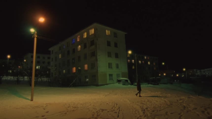 A man walks through a snow covered parking lot past an apartment complex