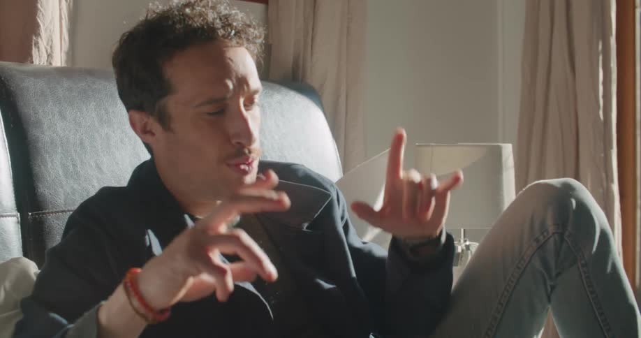Man reclining on bed gestures while talking via laptop