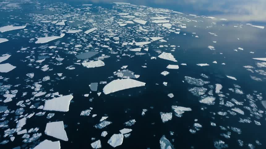 Broken pieces of ice are scattered over an ocean near a mountain range