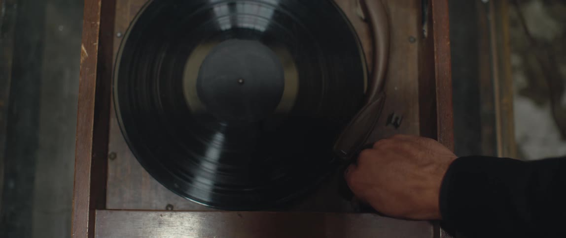 A vinyl record is on an old turntable and someone places the needle back at the beginning and turns it on