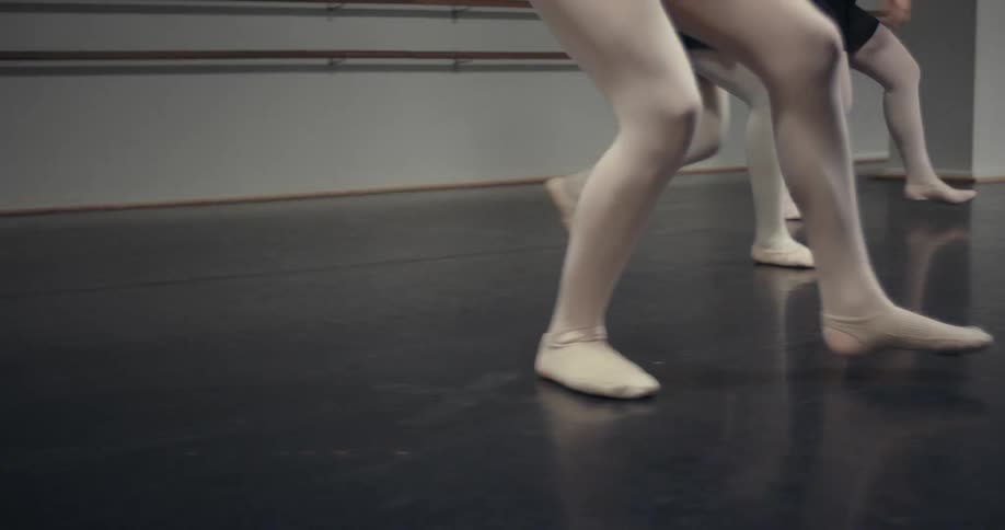 View of the feet of women wearing ballet slippers dancing on a hardwood floor