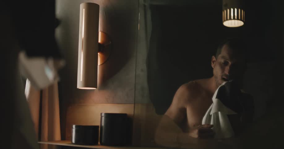 Man wipes his face while looking at his reflection in the bathroom mirror