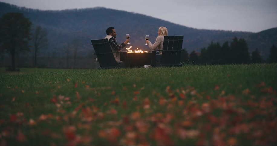 Couple drinks wine outside by fire in the fall