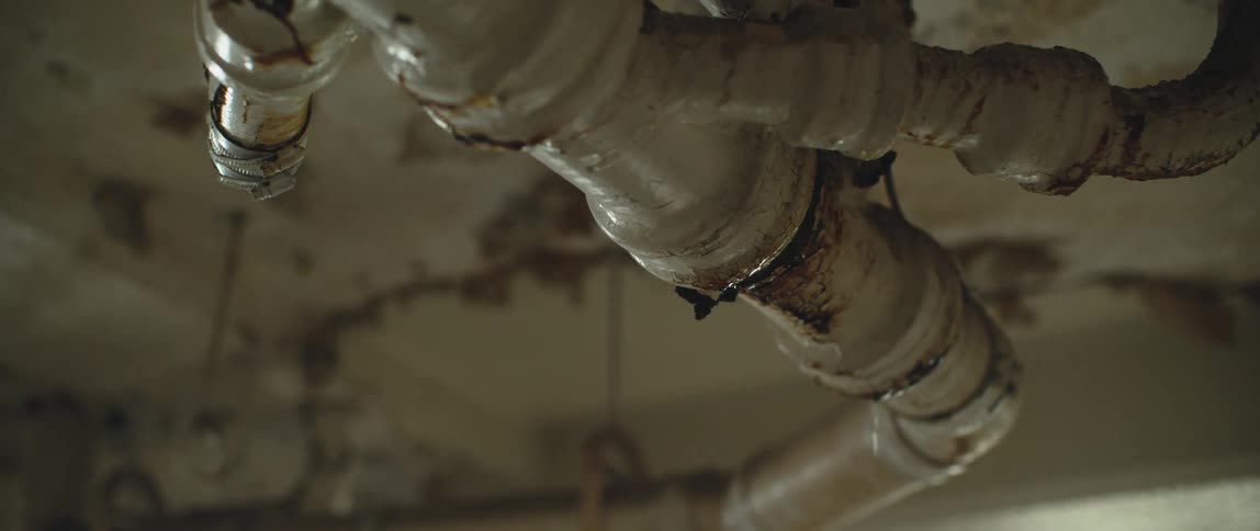 Old pipes on the ceiling of a room in an abandoned building leaking water