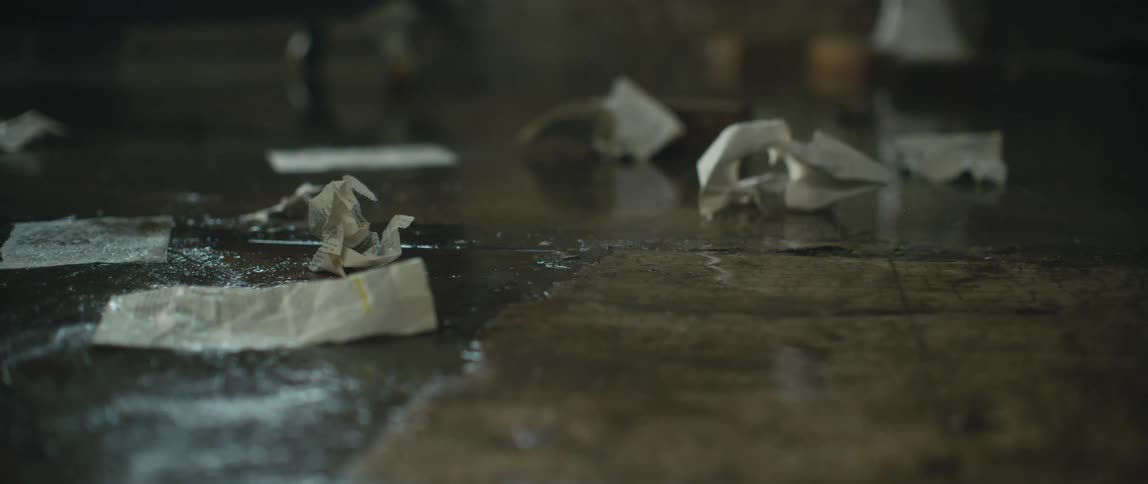 A man with bare feet walks back and forth on a sidewalk dropping crumpled papers in the rain