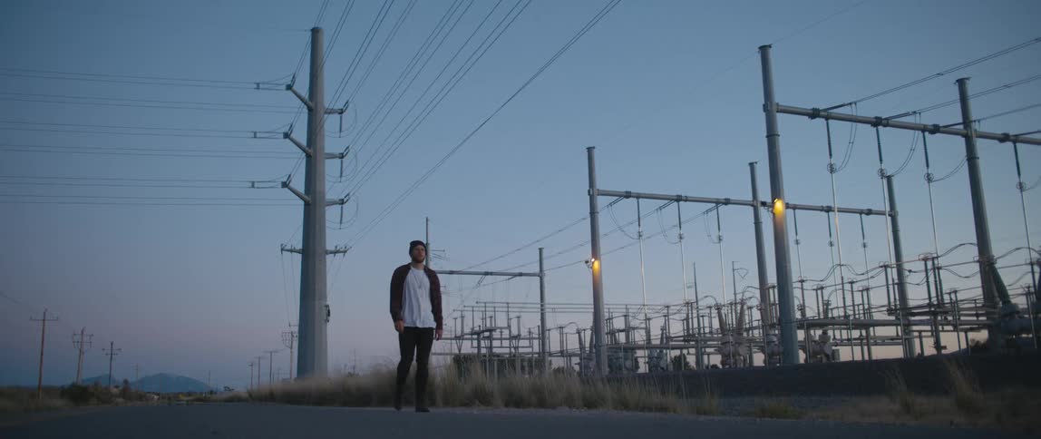 Man wearing a toque walks down a road past hydro poles at dusk