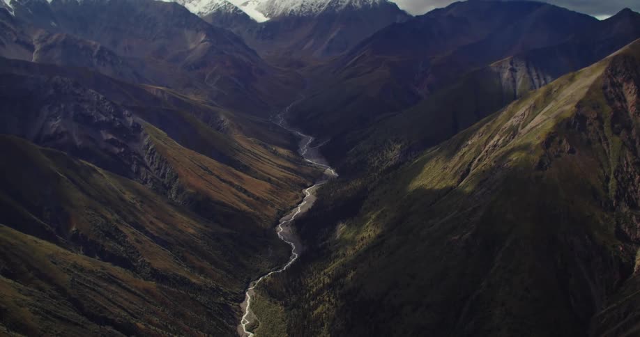 Water flows through valley between green slopes and away from snow capped mountains