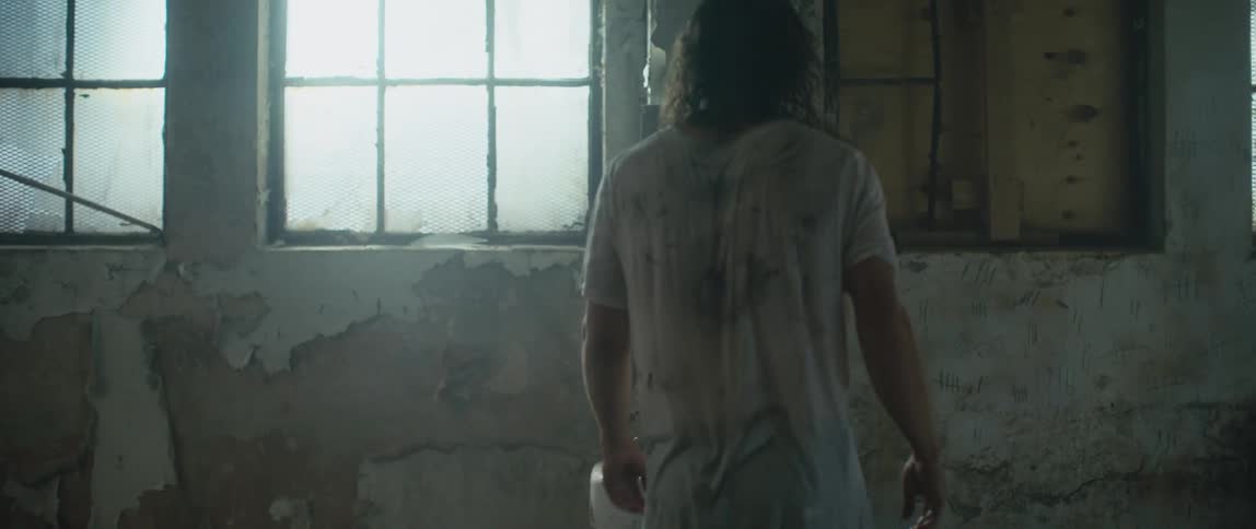 Man wearing dirty shirt walks to sink in abandoned building with peeling paint and hits wall