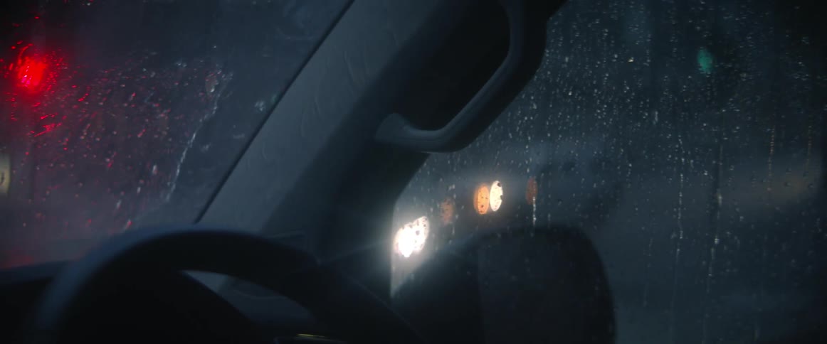 A vehicle waits at a busy intersection on a rainy night