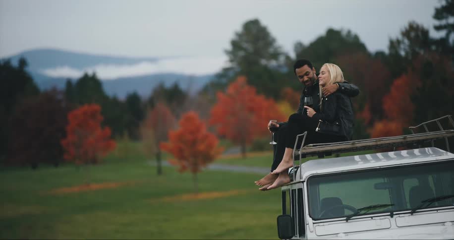 Couple sits on car drinking wine in the blue ridge mountains will fall color
