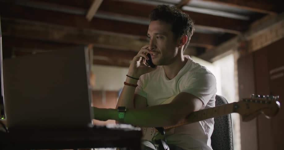 A man with a guitar recording it and talking on the phone